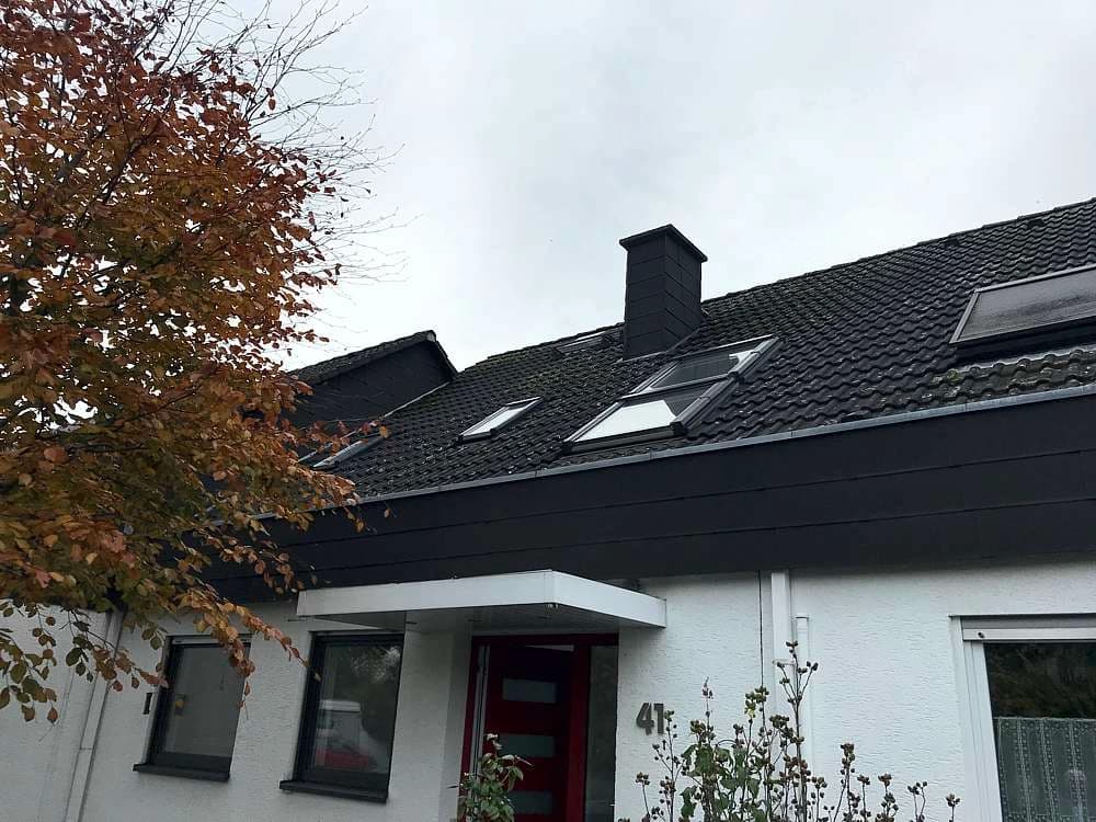 Einfamilienhaus mit dunkel eingedecktem Satteldach, Dachfenstern und Schornstein an einem bedeckten Herbsttag